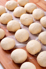 Yeast dough balls on the wooden board with flour. Proofing to bake buns, bread or pizza 