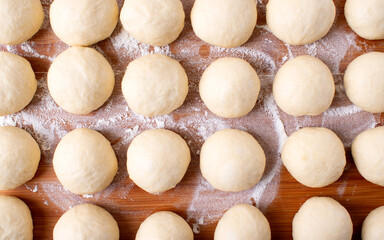 Yeast dough balls on the wooden board with flour. Preparing to bake buns, pizza or bread. Top view - 457875915