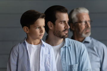 Close up profile three generations of men standing in row on grey studio wall background, looking in distance, serious 7s boy with father and senior grandfather dreaming, visualizing future