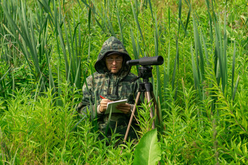 ornithologist records the results of the observations while standing among the tall grass in the wetland
