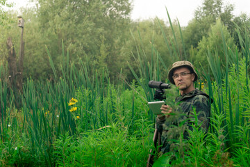 ornithologist with a spotting scope and notepad among the tall grass in the valley