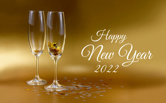 Happy New Year 2022 shiny golden background with glass of champagne stock images. Two festive glasses of champagne photo images. Happy New Year 2022 golden greeting card. New Year celebratory toast