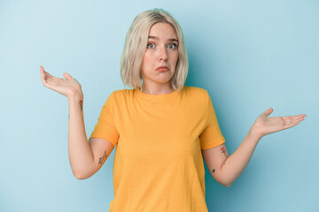 Young caucasian woman isolated on blue background doubting and shrugging shoulders in questioning...