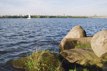 White sailboat floating in a pond with stones in the foreground in Yekaterinburg