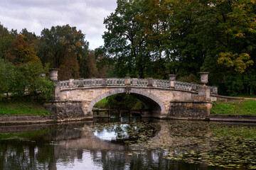 Fototapeta premium View of the Slavyanka River and the Viscontiev Bridge in the Pavlovsk Palace and Park Complex on a cloudy autumn morning, Pavlovsk, Saint Petersburg, Russia