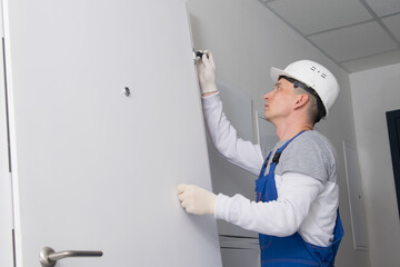 a carpenter in uniform, adjusts the hinges of the front door, there is a place for the inscription