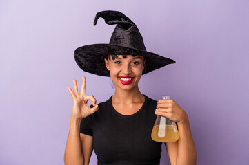 Young mixed race woman disguised as a witch holding potion isolated on purple background  cheerful...