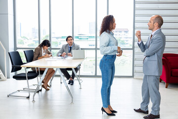 Businessman and businesswoman sharing laptop while standing in office building room.