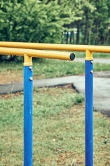 Fototapeta premium Yellow metal bars for exercises with hanging rain drops at sports ground in spring green park on cloudy day extreme close view