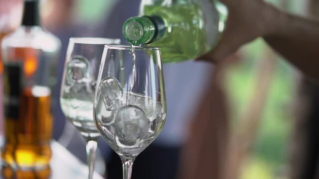 Bartender mixes alcoholic cocktails at bar pours from bottle into glass with ice