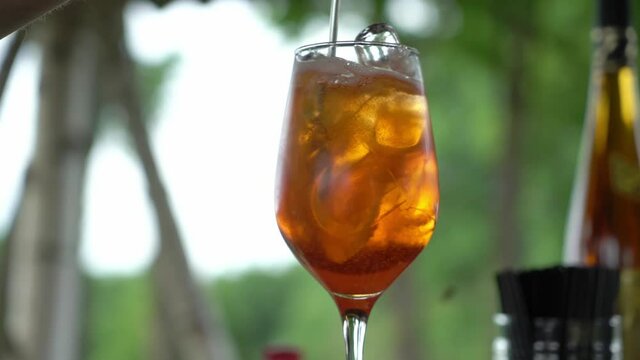 Mixing italian cocktail Aperol Spritz in glass. Drink in summer bar outdoors.