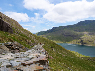 Low angle view of flat stone path on lakeside called Miners Track in Snowdonia mountains leading to Snowdon mount.