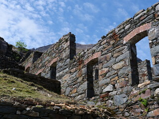 Stone wall of decaying building with no roof in the mountains on a sunny day.