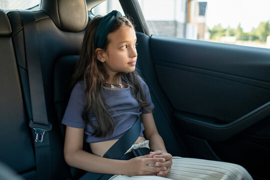 Little girl sitting on backseat of new comfortable electric car and looking through window