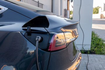 Side view of back part of black electric car with plugged charging cable at fueling station