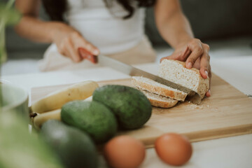 Close up of healthy woman hands cutting whole wheat bread. Young woman cooking healthy food at home. Healthy and wellness concept.
