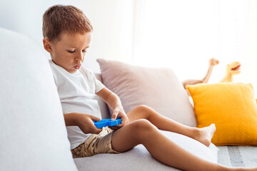 A small child is sitting on the sofa and holding a pop it toy. Portrait of concentrated cute little...