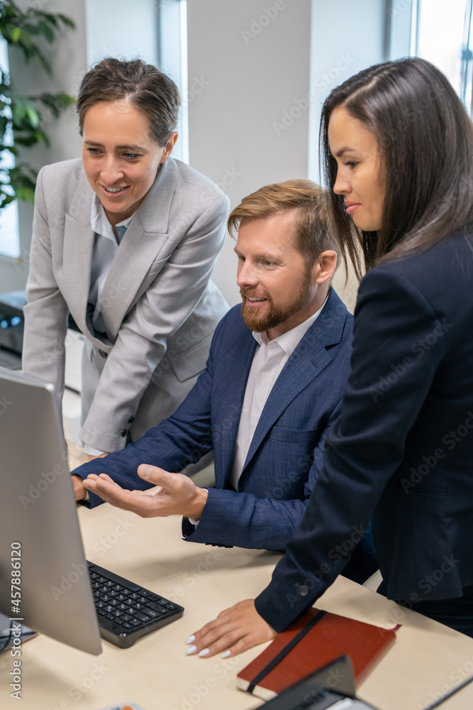Poster three young office workers in suits looking at computer screen during presentation