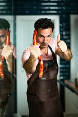 Young handsome man holding sausage, in hands.
Chef and he’s meat products, in a kitchen. 