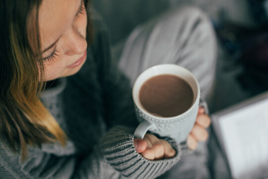 Young girl drinking winter beverage hot cacao, sitting on cozy bed, reading book. Cozy warm image