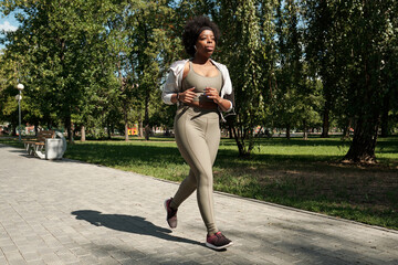 Contemporary young plus size African female in activewear jogging in park on sunny morning