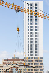 yellow tower crane lifts metal reinforcement against the backdrop of a high-rise building under construction. Construction site and construction of apartments.