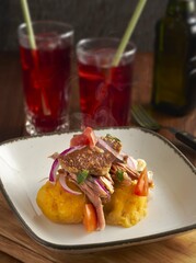 Plato de hornado con tortillas de papas fritas, piel de cerdo crujiente en salsa de agrio y mote tradicional, con agua de Jamaica en el vasos de cristal