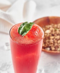 Vaso de jugo de sandía con hoja de albahaca y plato de granola desenfocada