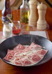 Raviolis rosados de salmon en salsa blanca con queso mozzarella sobre plato negro profundo