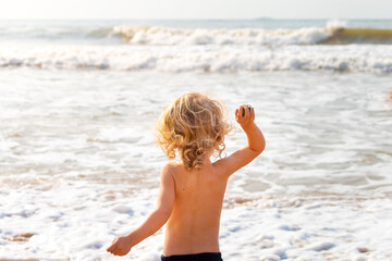 CRIANÇA LOIRA DE 2 ANOS, LOIRO, USANDO CALÇÃO DE BANHO, BRINCANDO NA PRAIA EM UM AMANHECER.
