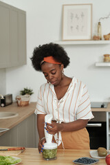 Fototapeta na wymiar Young female bending over kitchen table while preparing fruit smoothie