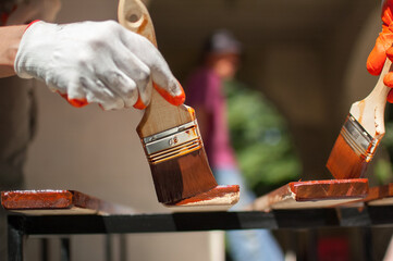 Female worker makes painting works of wooden products, plank with brown paint for making bench, carpenters work, wood covering protection.