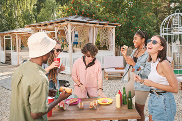 Happy young friends having fun by table with snacks while enjoying summer day