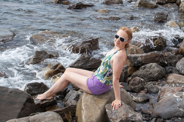 young girl sitting on coastal stones by the sea