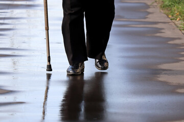 Woman walking with a cane on a wet street, female legs in on sidewalk after rain. Concept of disability, limping person, diseases of the spine, old people