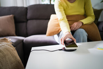 Fototapeta premium Charging mobile phone battery with wireless charging device in the table. Smartphone charging on a charging pad. Mobile phone near wireless charger Modern lifestyle technology concept.