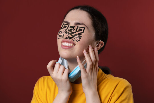 Portrait of a woman with a QR code instead of eyes and nose, removing protective mask from her new face. Brown background. The concept of chipization and identification about the vaccine - Powered by Adobe