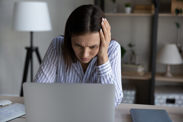 Unhappy young woman reading bad news in message, looking at laptop screen, worried frustrated...