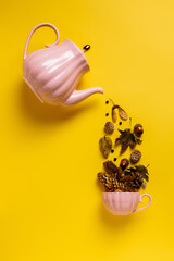 Creative layout with tea pot pouring autumn dry flowers, acorns and leaves into tea cup on vibrant yellow background. Creative fall season concept. Still life visual trend. Flat lay.	