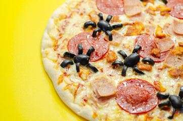 Meat feast pizza on thin dough decorated with black olives in the shape of spiders, food for Halloween party