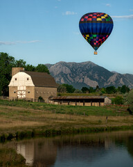 Fototapeta na wymiar A hot air balloon rise above a barn and the Flatirons near Boulder, Colorado 