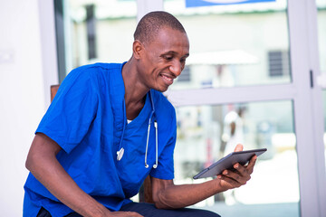 young male doctor working on a digital tablet while smiling.