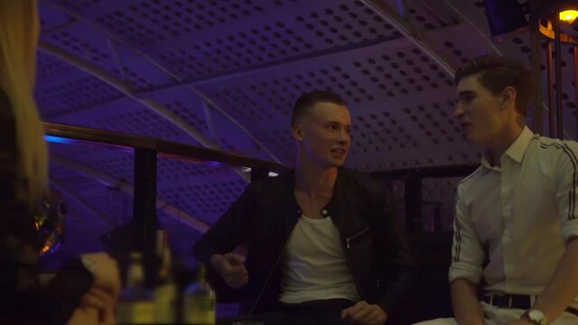 Guys and girls relax at a table in a nightclub. They laugh, drink, talk . Celebration of the holiday. A party. The concept is not a healthy lifestyle. Alcoholism.