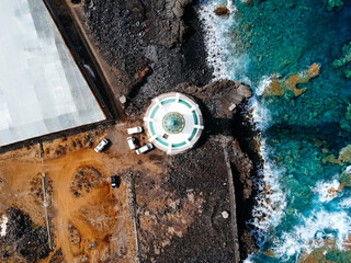 Aerial top view of lighthouse, rocks and ocean waves in a volcanic landscape