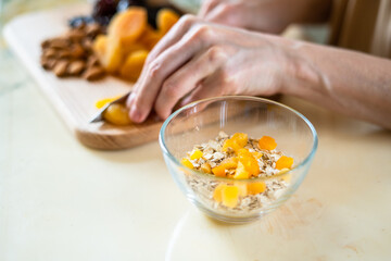 female hands cut dried fruits and nuts with a green knife: dried apricots, almonds and dates on a wooden cutting board into a glass bowl