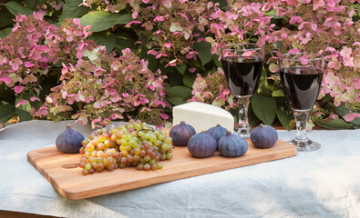 Wine, grape, figs and cheese on cutting board  on autumn hydrangea flowers background