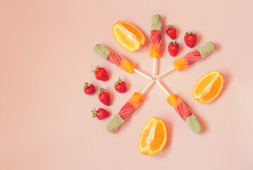 Spiral orange-strawberry popsicles and fresh fruits on pink background.