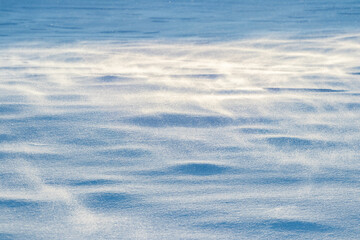 Snow-covered ground in sunlight, wind blowing snow, winter background