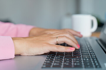 Close up of unrecognizable caucasian woman working with keyboard at home. Horizontal detail of woman hands typing on computer indoors. Online working and technology concept.