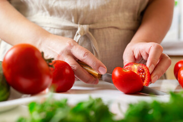 Chef slicing tomato using knife on the table in restaurant. Process of cutting and preparation food in kitchen.